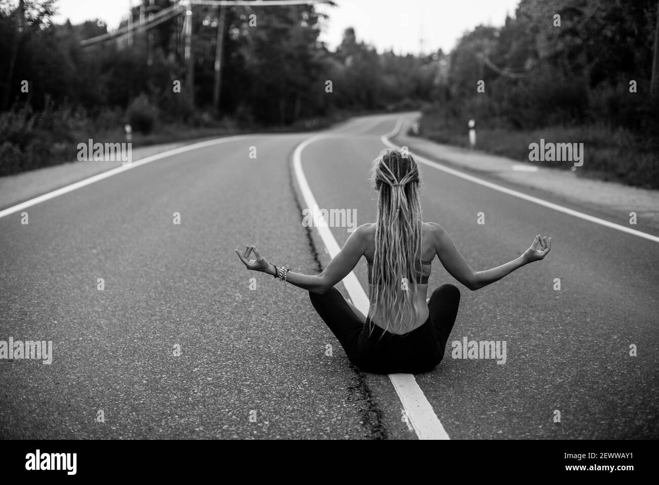 An yoga woman meditate sitting in the middle of the road. Black and ...