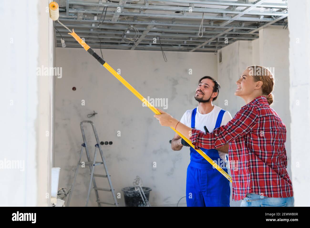 A man in overalls tells a woman how to paint a wall correctly Stock