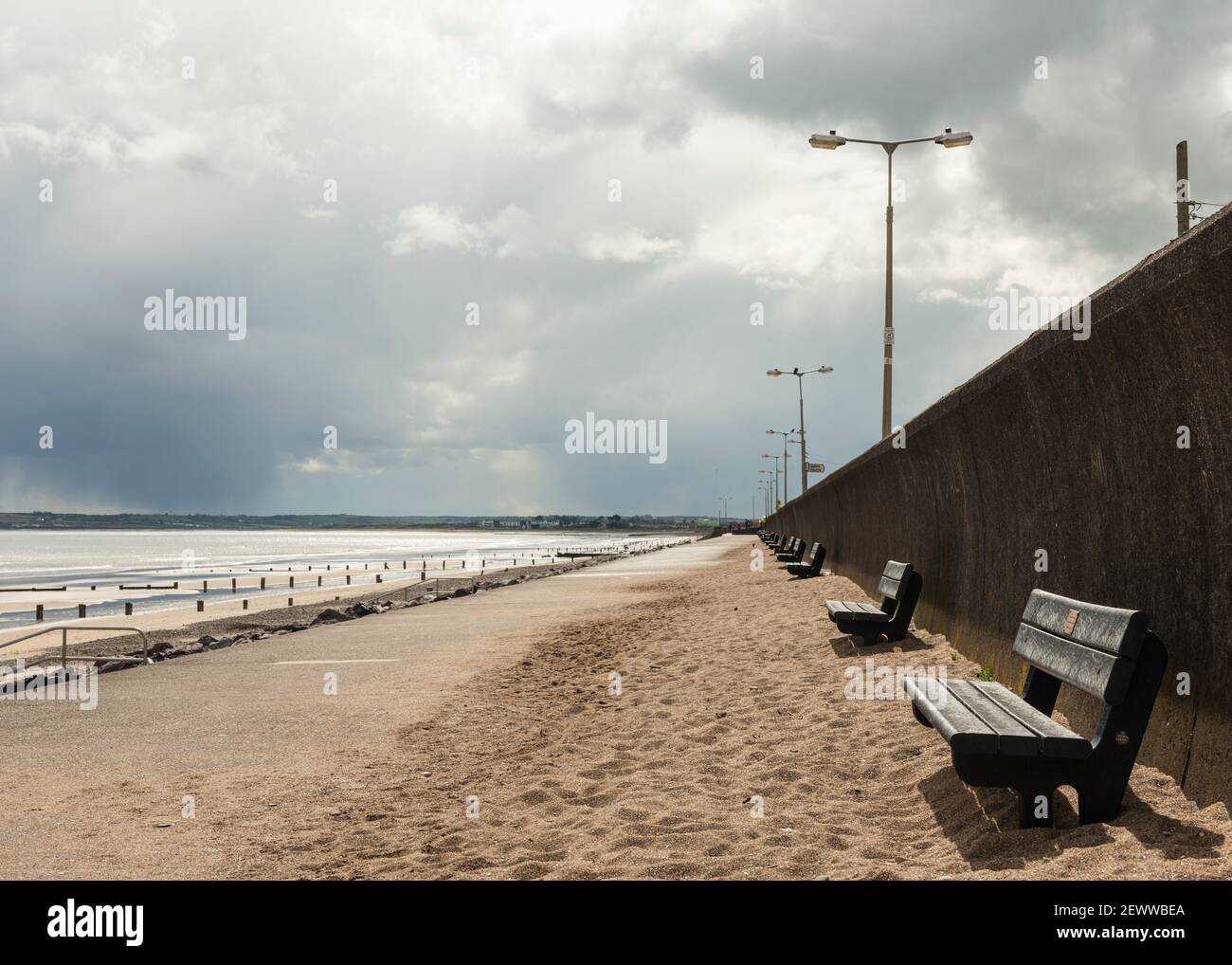 Empty benches on sandy promenade at the deserted empty Youghal Strand beach out of season in Youghal, County Cork, Ireland as of 2018 Stock Photo