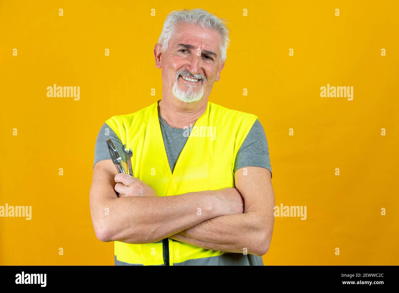 portrait of a mature worker wearing reflector vest showing tools isolated on yellow background Stock Photo