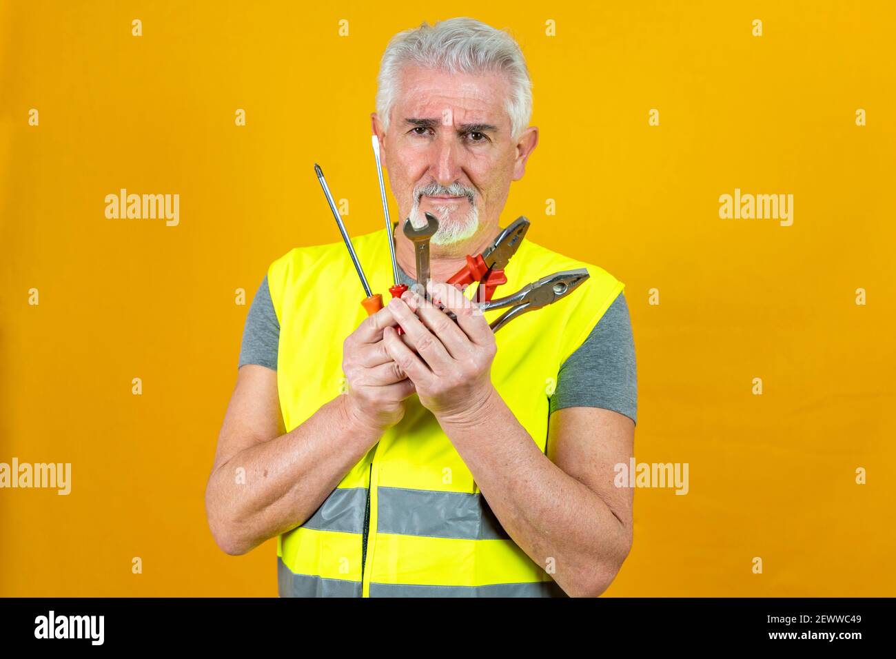 portrait of a mature worker wearing reflector vest showing tools isolated on yellow background Stock Photo