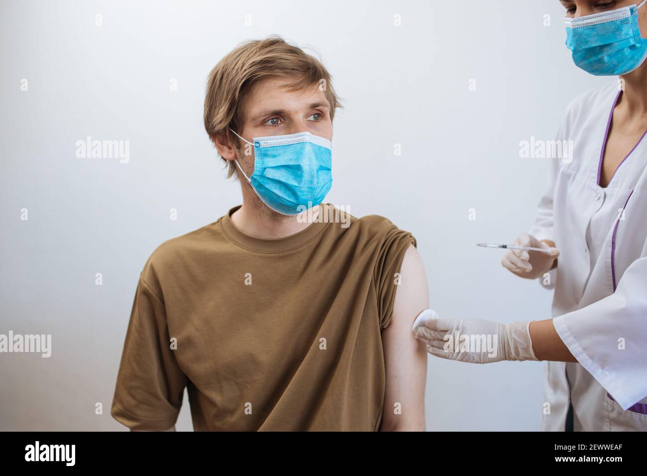 Male getting Covid-19 vaccine. Close up doctor making injection to patient in medical mask. Syringe of coronavirus vaccine. Man receives jab vaccinate Stock Photo