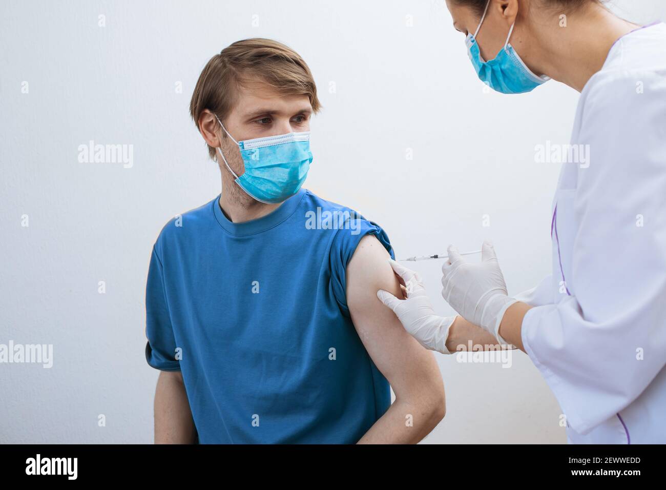 Male getting Covid-19 vaccine. Close up doctor making injection to patient in medical mask. Syringe of coronavirus vaccine. Man receives jab vaccinate Stock Photo
