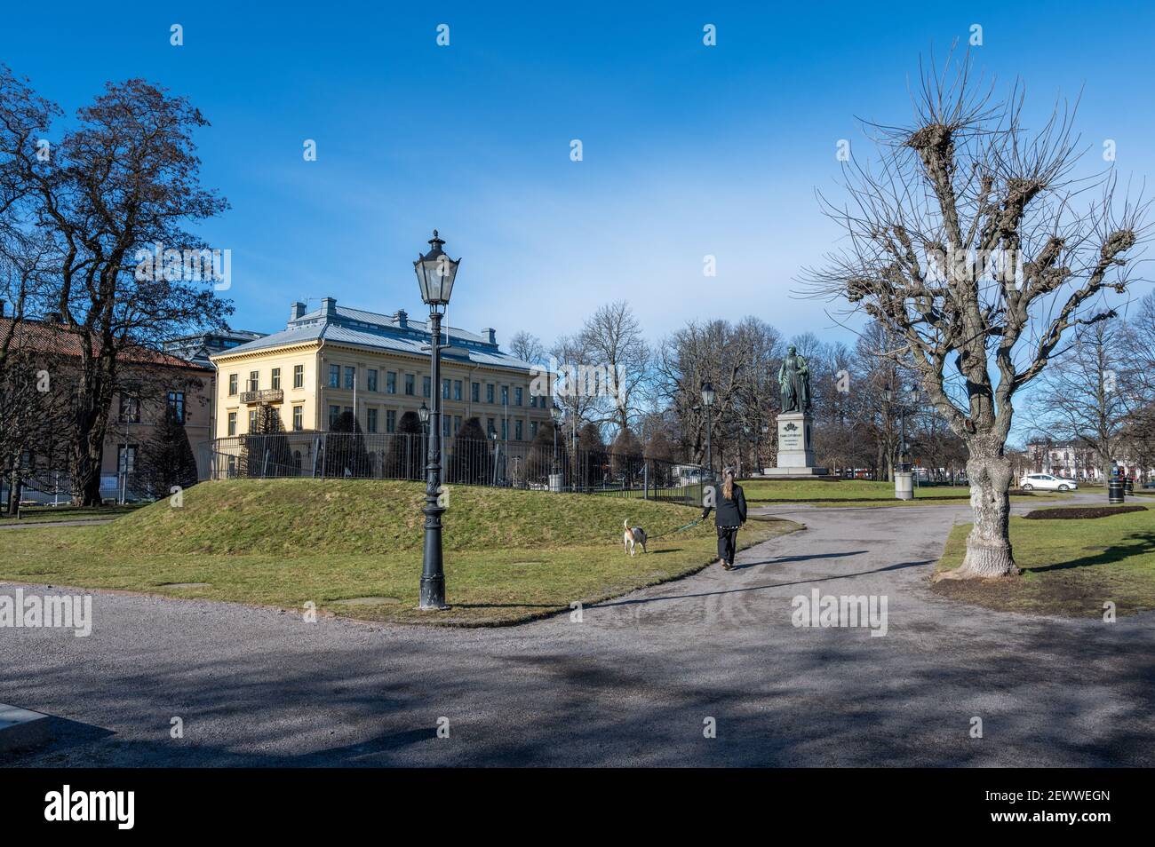 Unrecognizable person walks a dog in Carl Johans park with the statue of king Karl Johan XIV during an early spring day in Norrkoping, Sweden. Stock Photo