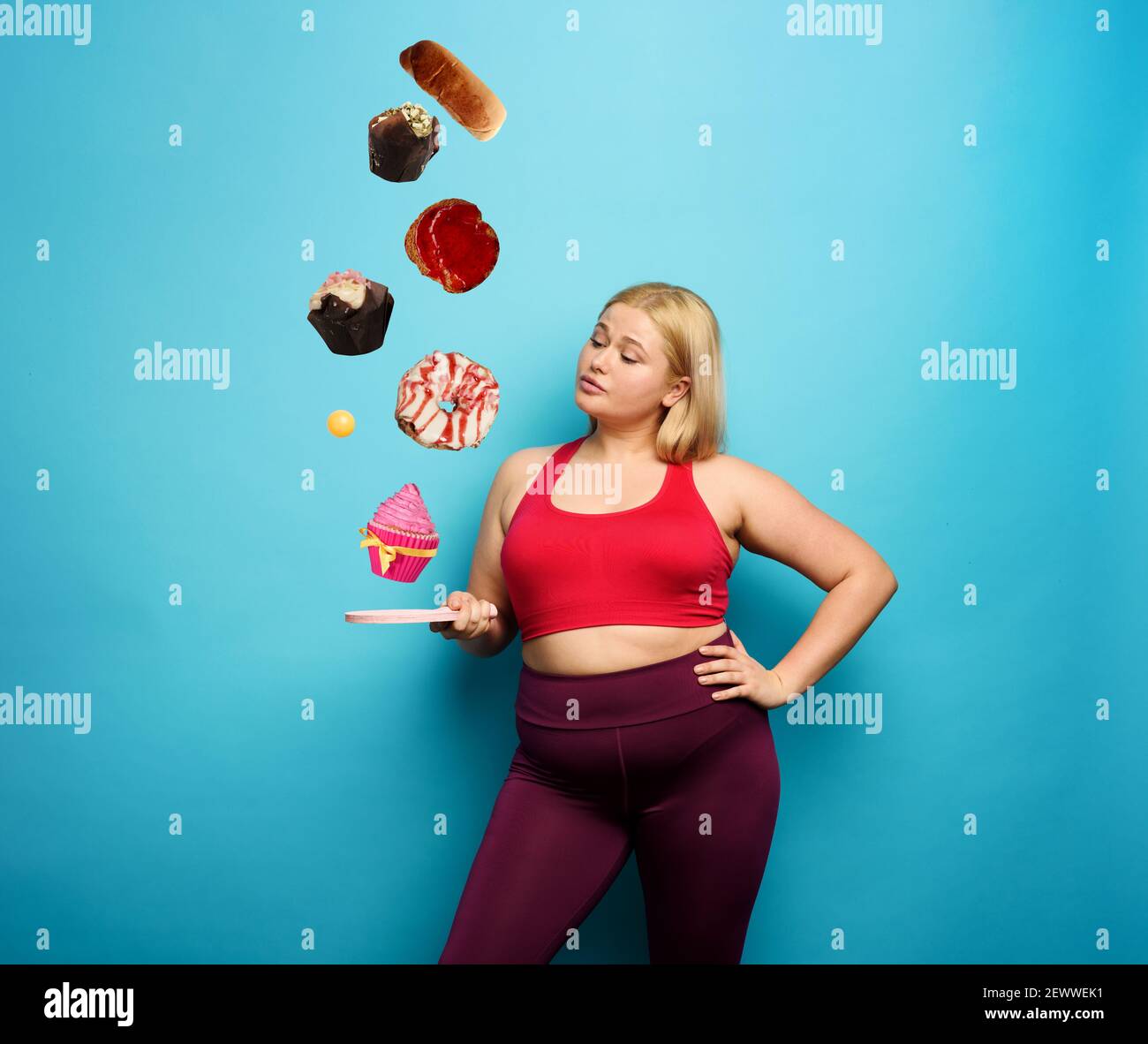 Fat girl tries to play with table tennis but thinks always to eat. Cyan background Stock Photo