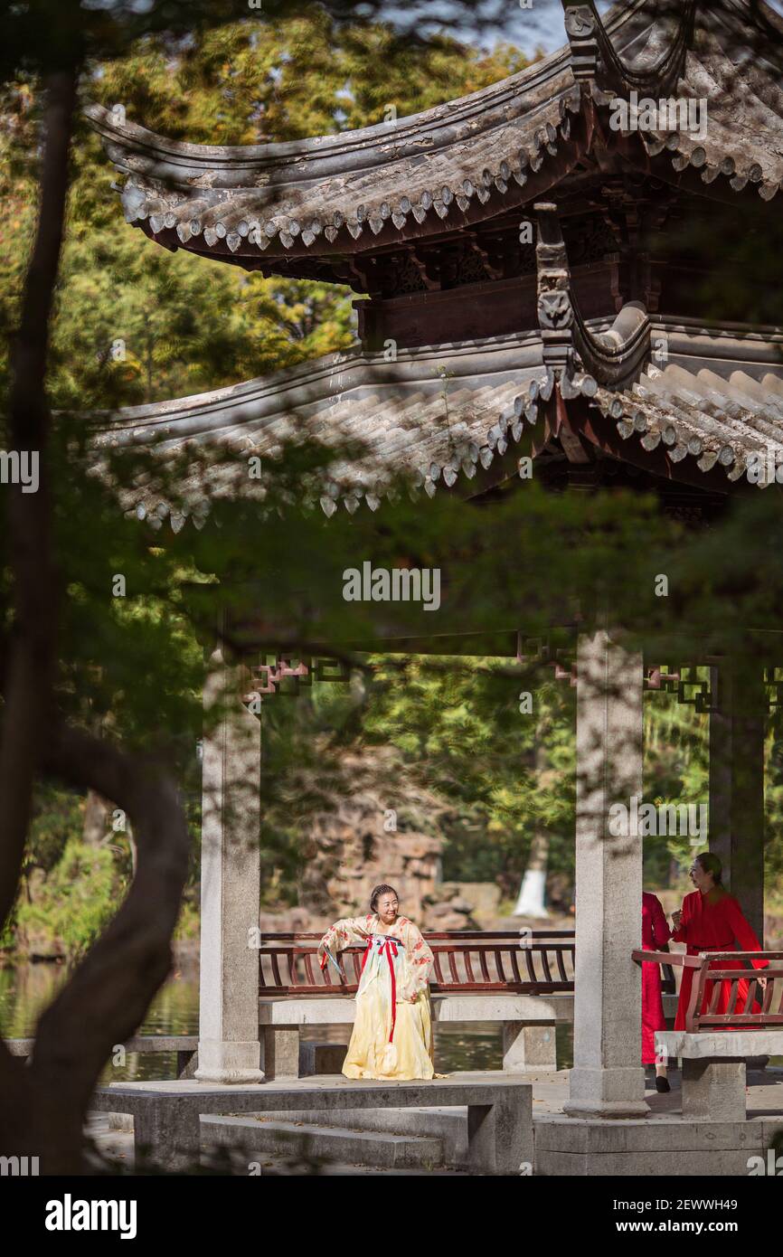 Huzhou, China, 18 November 2020: Chinese woman wearing traditional dress and holding fan in park in China. Happy Spring Festival, Chinese New Year Stock Photo