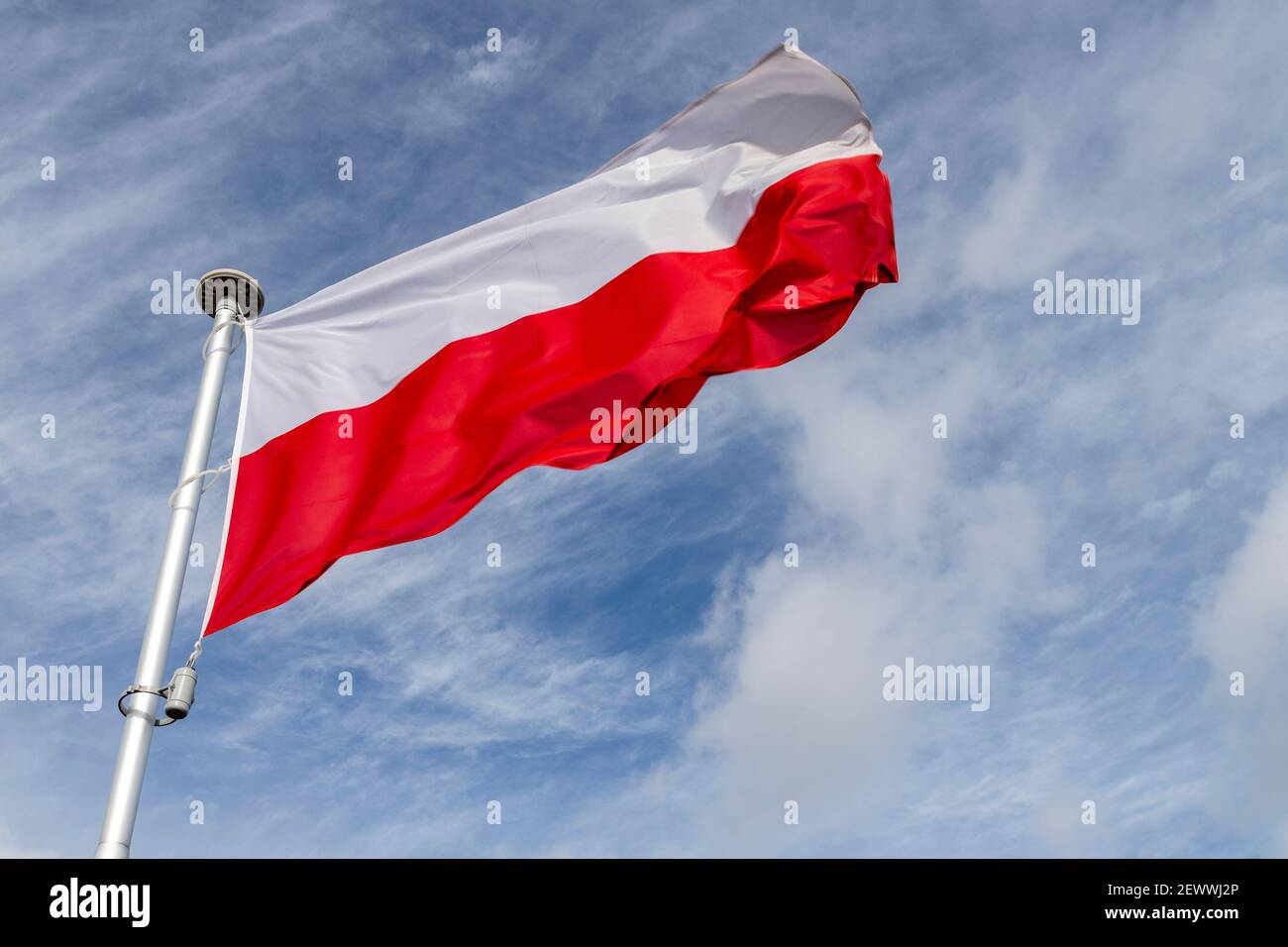 Polish flag on a background of the cloudy sky. National symbol of Poland on the mast. Summer season. Stock Photo