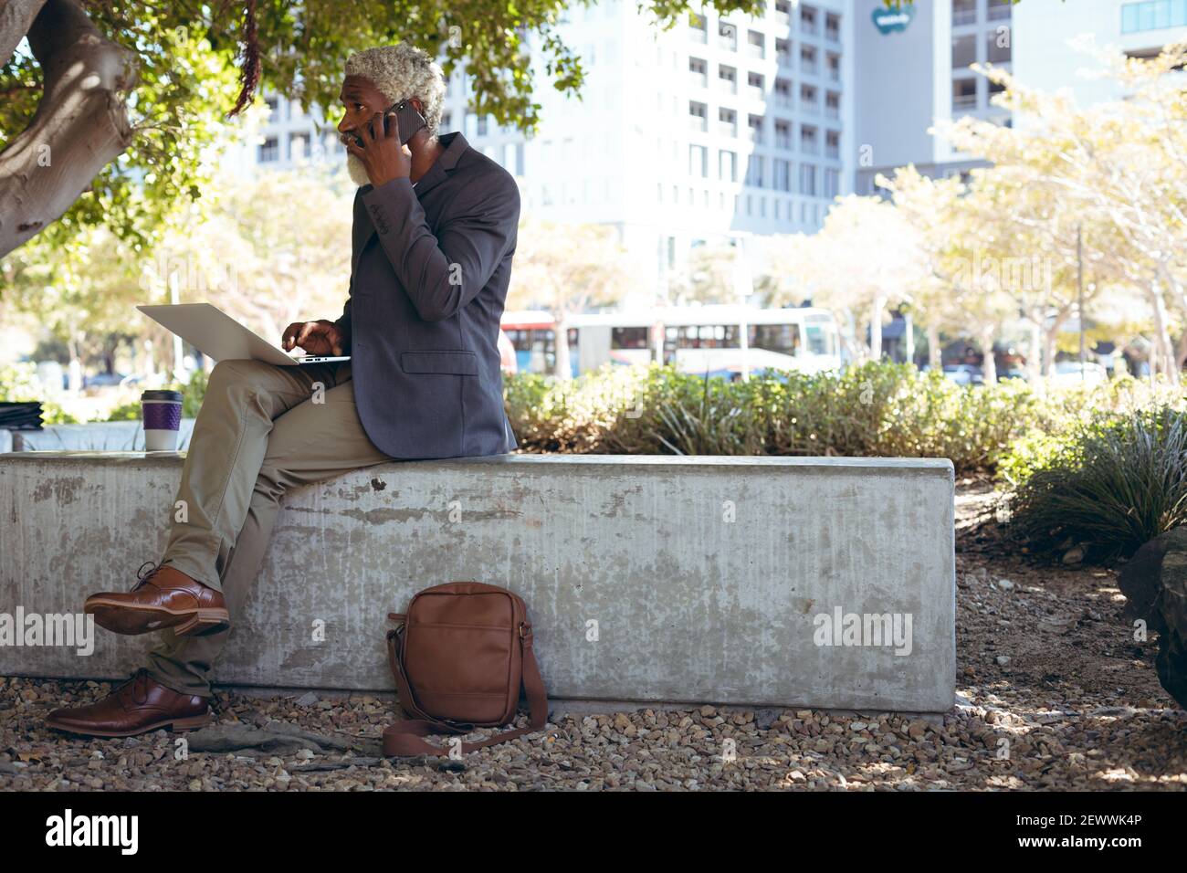 African american senior man sitting on wall in street using laptop computer Stock Photo