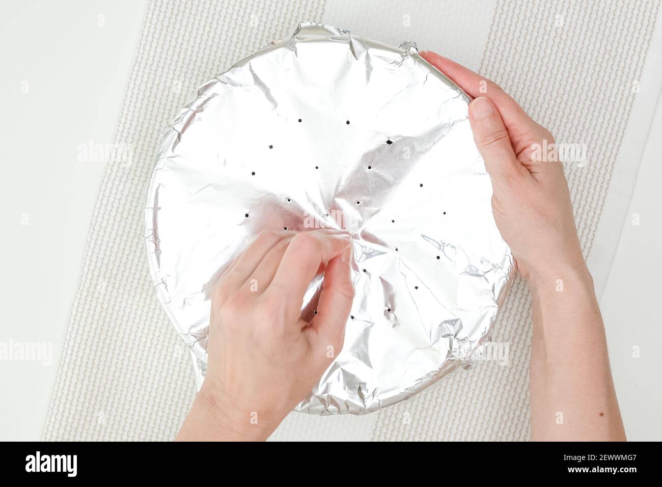 Woman hands making little holes in aluminum foil after covering baking pan. Step by step baking process, recipe. View from above, copy space Stock Photo