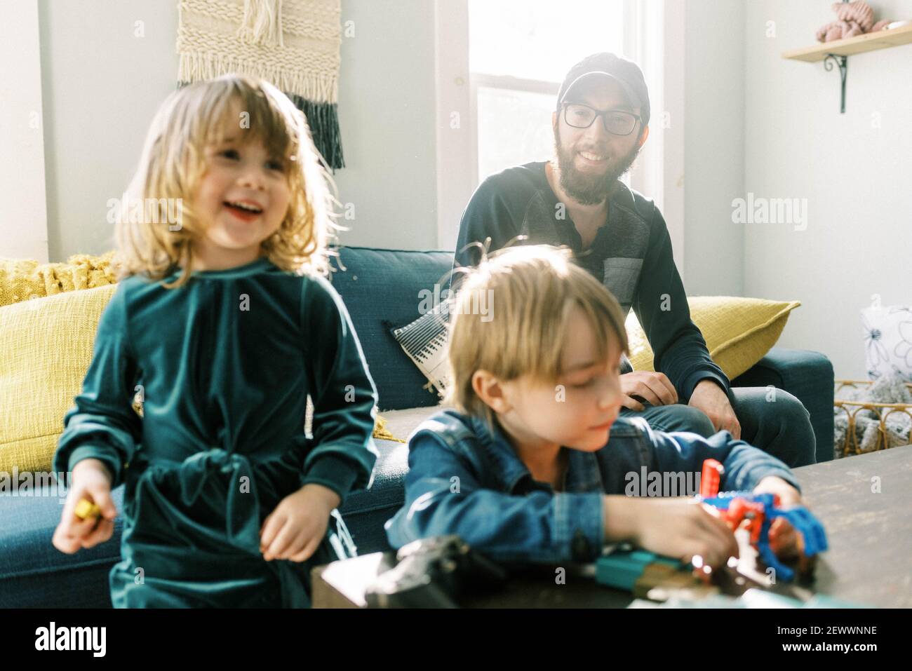 A father looking at his playing children lovingly in sunny room Stock Photo