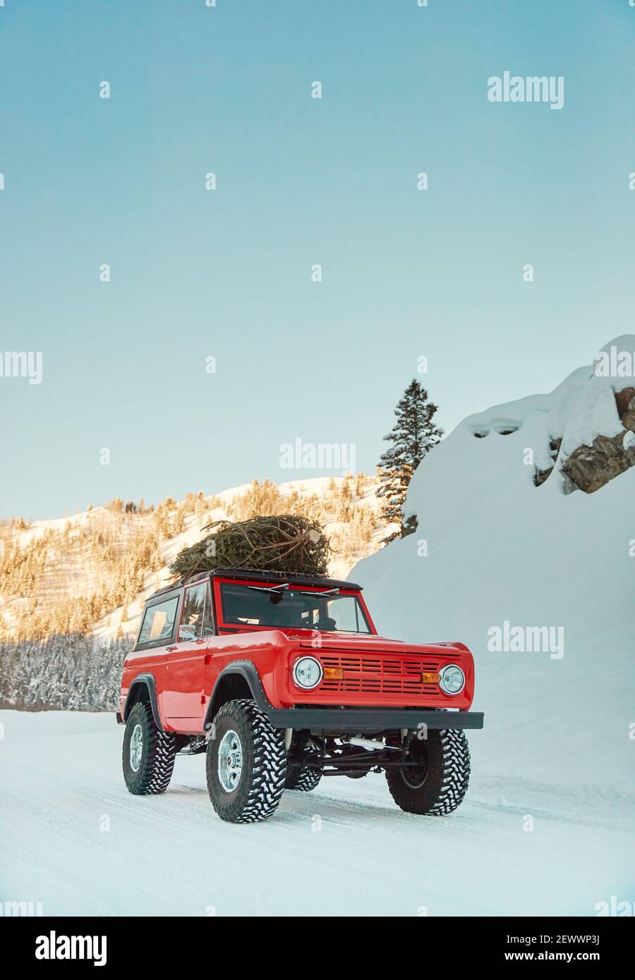 SUV with Christmas tree on roof drives down snowy mountain road Stock Photo