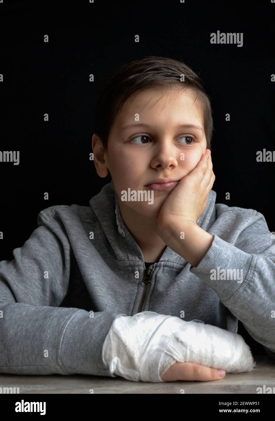 portrait of boy with plaster cast on his hand in front of black wall Stock Photo
