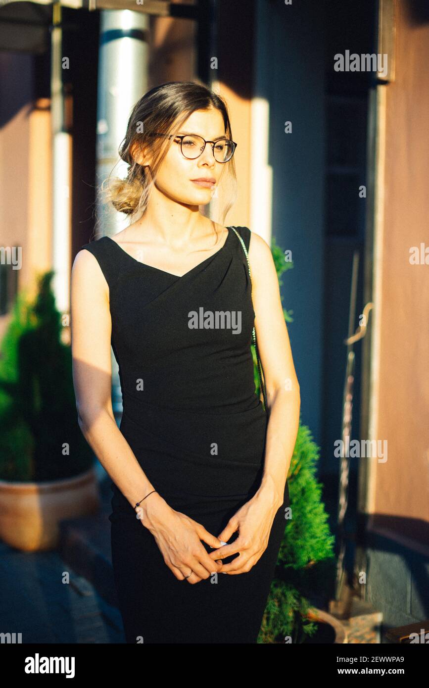 Young woman in black dress and glasses in the sunny city Stock Photo