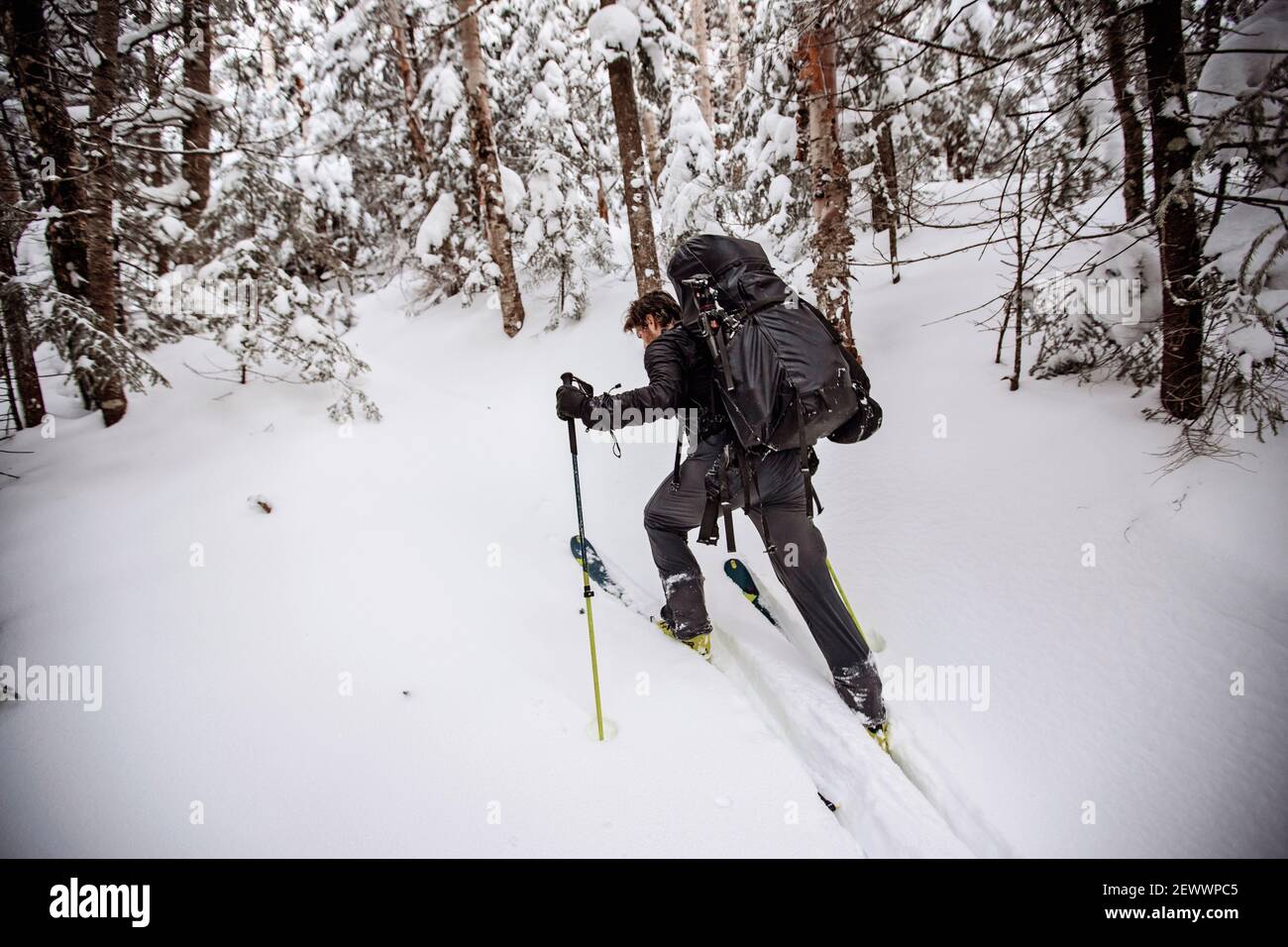 Make skier struggles with heavy pack skinning uphill in snow Stock
