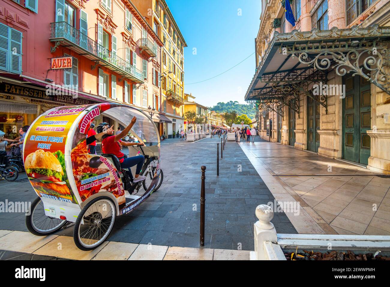 A female cyclist taxi driver guides tourists on a 3 wheel rickshaw bicycle through the Old City of Nice, France on the French Riviera. Stock Photo