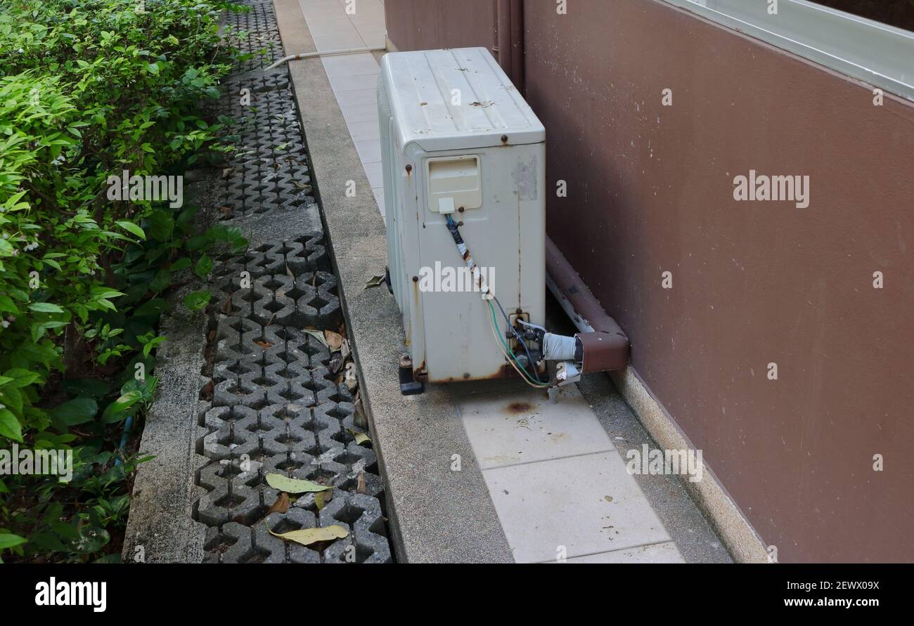 Connection of weathered electrical wires and refrigerant duct at rusty condensing unit outside a building Stock Photo