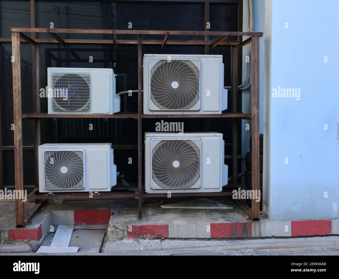 Closeup stack of condensing units installed on metal frame structure standing on sidewalk outside a building Stock Photo