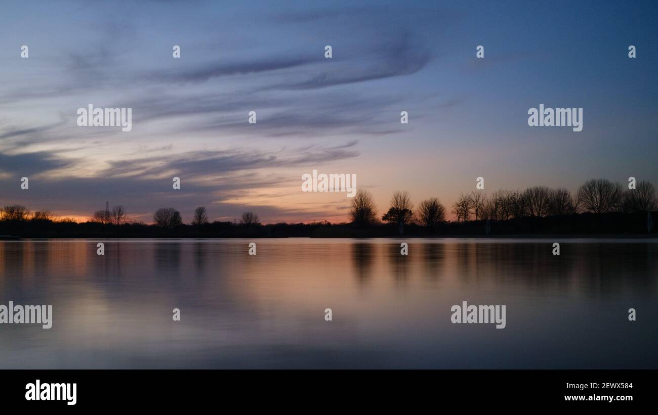 A lake reflecting trees in a park during a scenic cloudy sunset Stock ...
