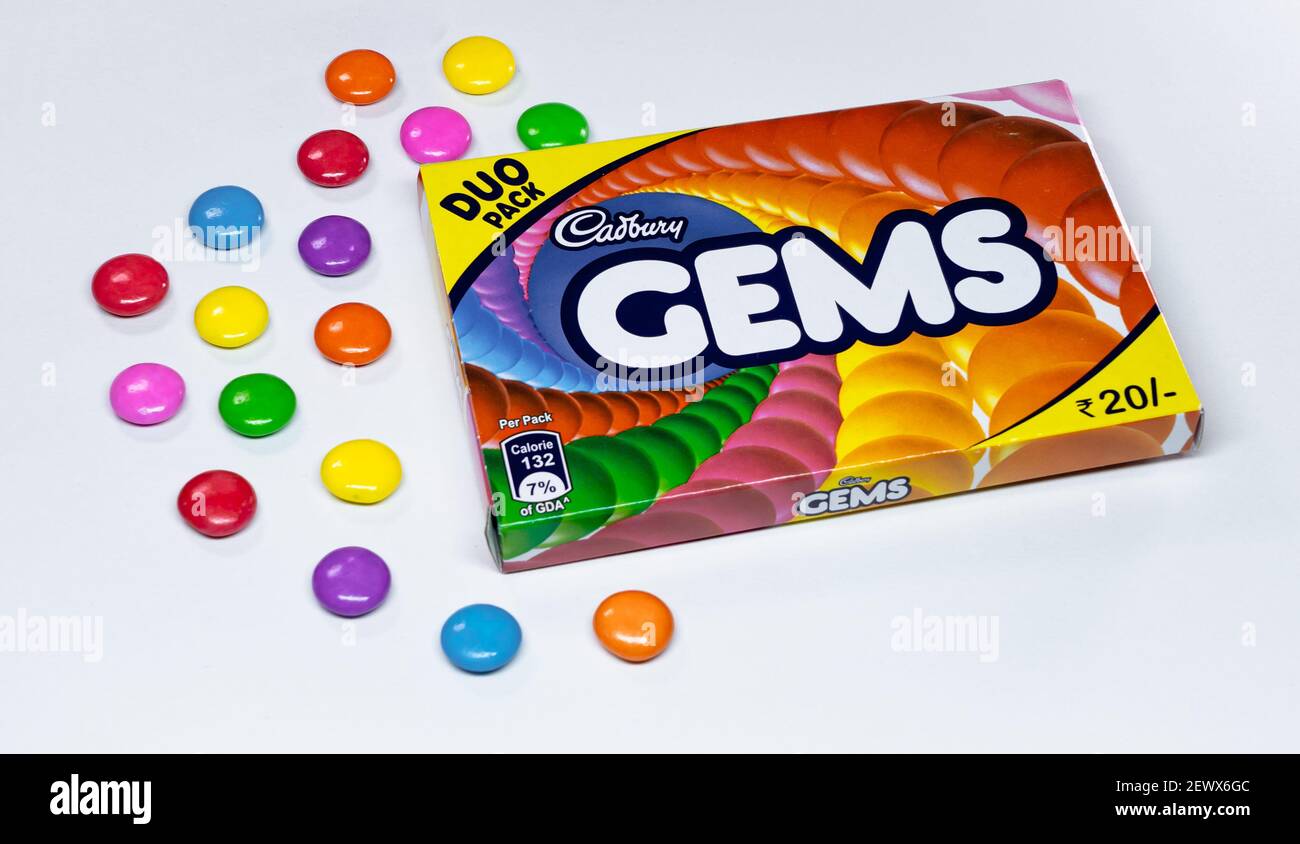 A box of Cadbury Gems and colorful milk chocolate buttons placed on a white paper background. Stock Photo
