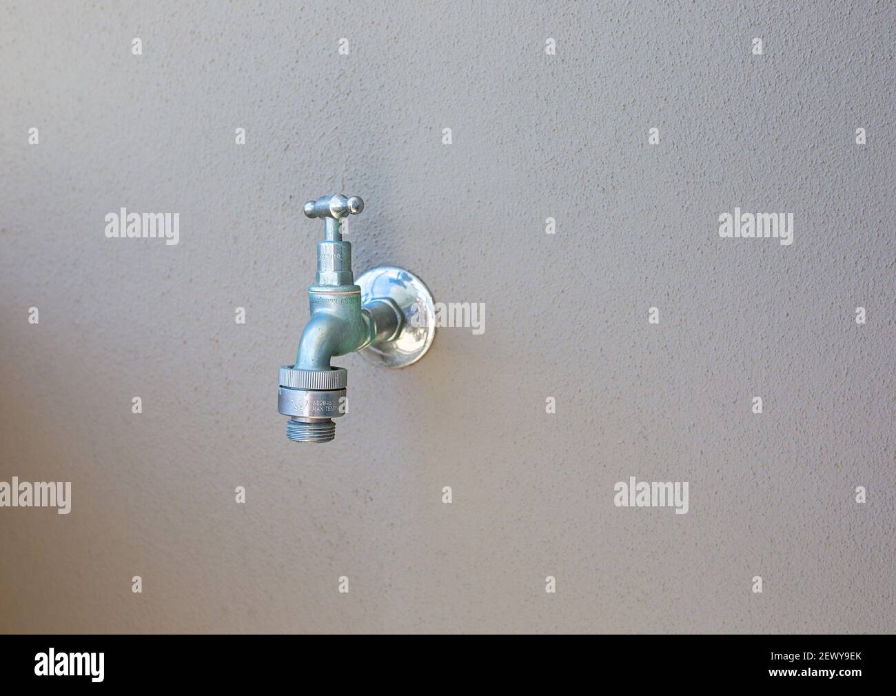 Outdoor tap with hose connection against a plain rendered wall Stock