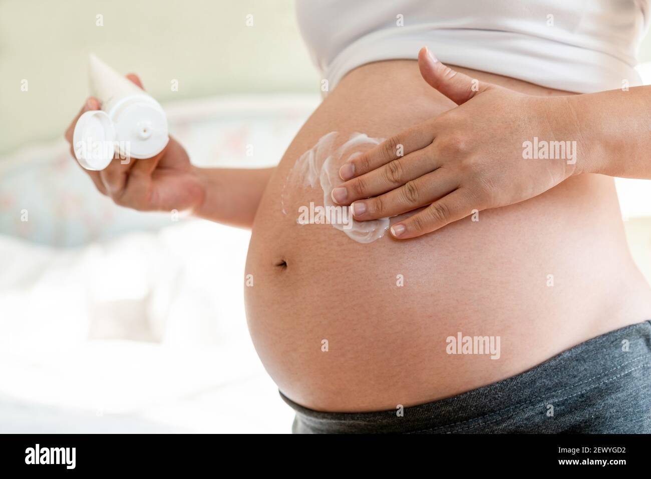 Happy pregnant woman apply skincare cream lotion on pregnant belly to