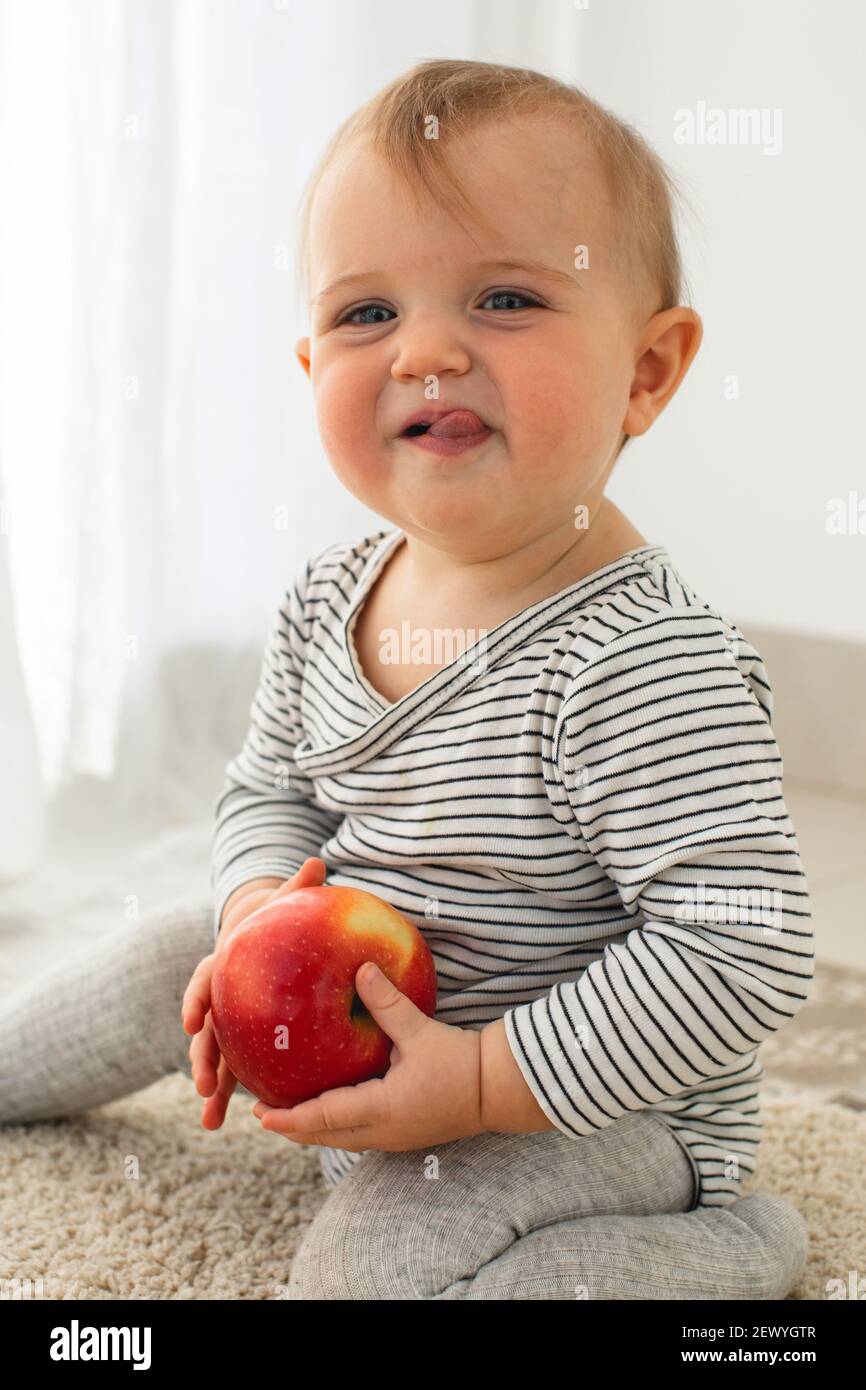 Cute baby girl are sitting with apple white background interior. Funny child explores the fruit Stock Photo