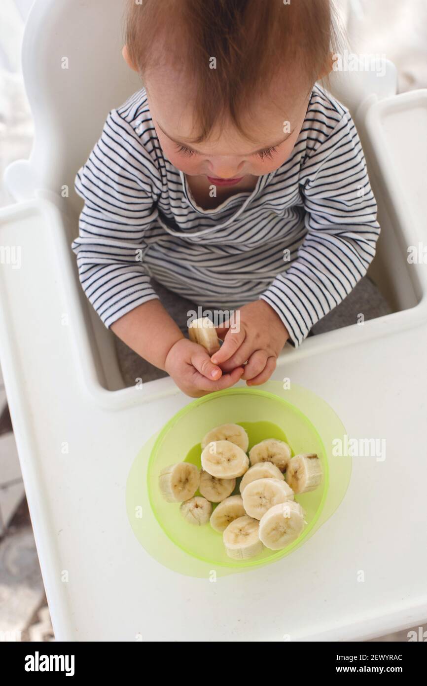Cute baby girl are sitting whith sliced banana white background interior. Funny child explores the fruit top view Stock Photo