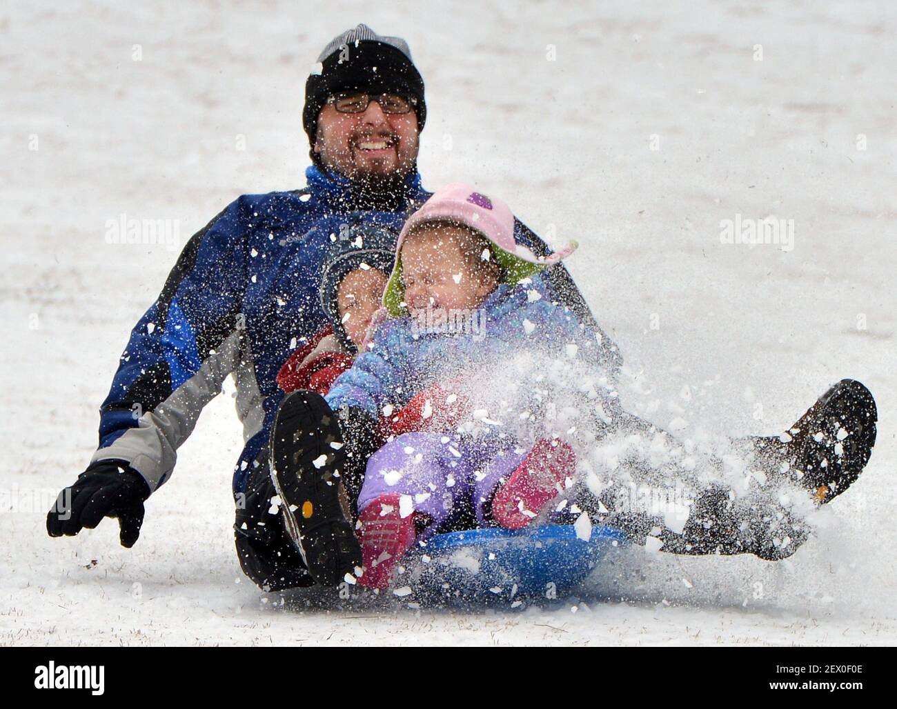 Hussein Genk, left, gets a fateful of snow as he flies down a hill on a sled with his children Kareena, 2, front, and Ayyub, 4, on Tuesday, Feb. 17, 2015 in Durham, N.C. A winter storm that made it's way across the region Monday night made roads and sidewalks hazardous. (Photo by Chuck Liddy/News & Observer/TNS) *** Please Use Credit from Credit Field *** Stock Photo