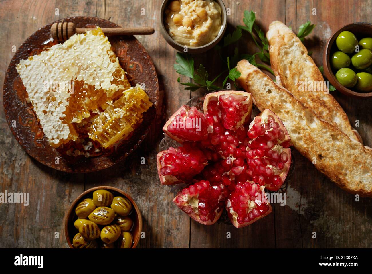 From above half of pomegranate and sweet honeycomb placed on wooden rustic table near olives and baguette toast with hummus Stock Photo