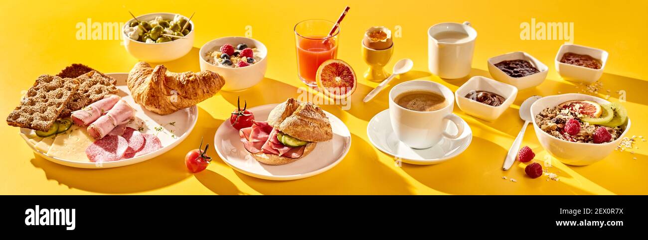 High angle of assorted yummy food and beverages served for breakfast in morning on vivid yellow background Stock Photo