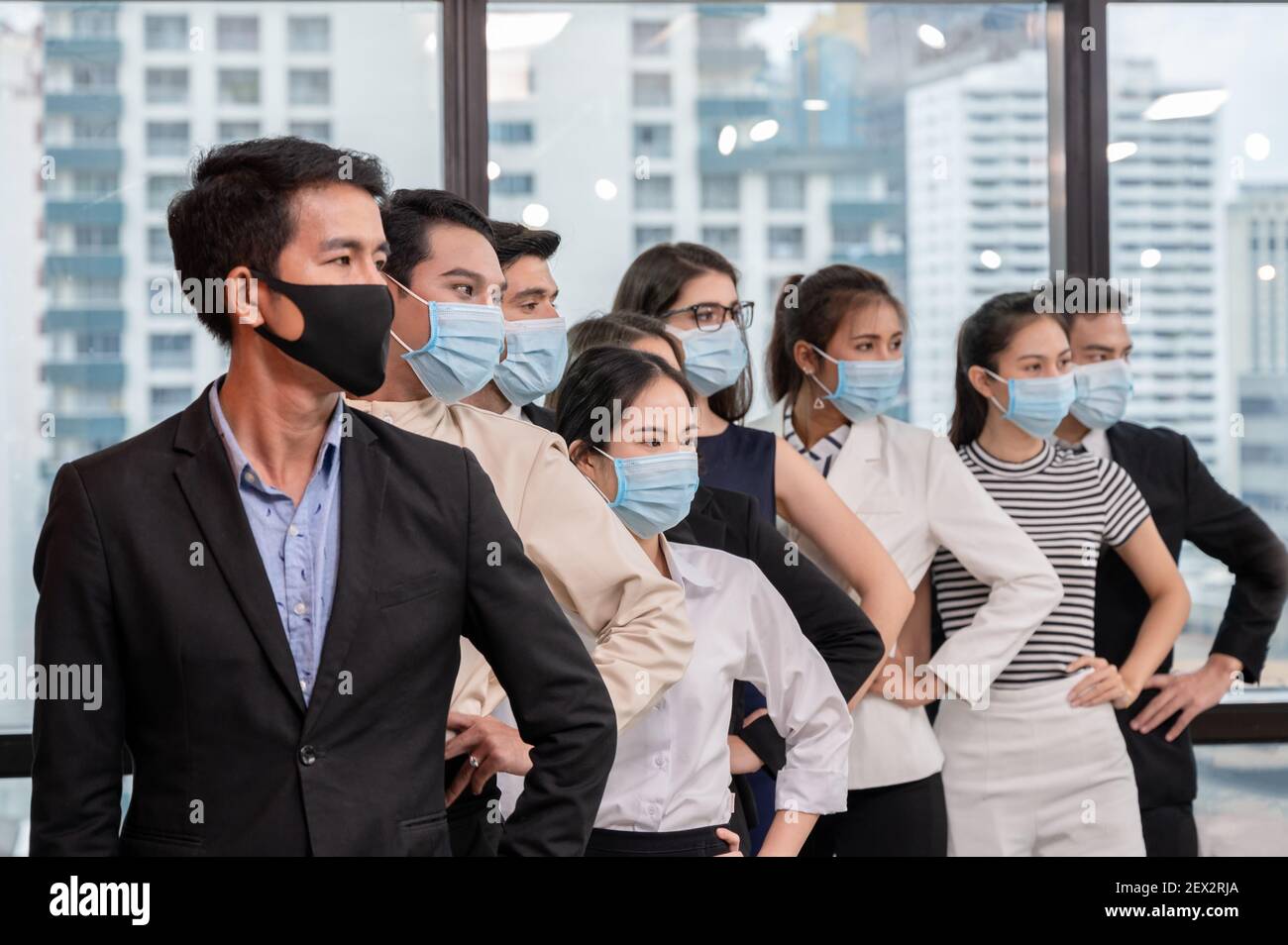 Row of multiethnic business group wearing face mask gesturing arm akimbo in new normal office while pandemic of coronavirus, covid 19 Stock Photo