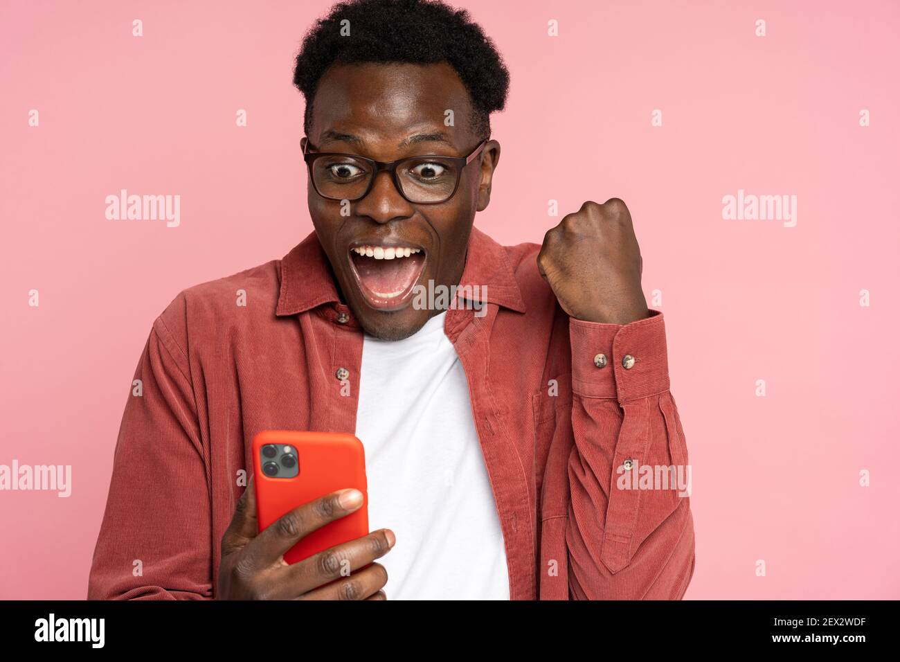 Overjoyed Black male look at smartphone, smile feel joyful reading good news, doing winner gesture Stock Photo