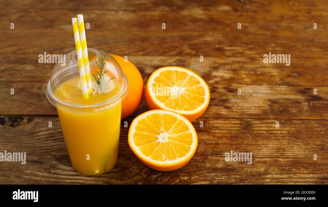 Orange juice in fast food closed cup with tubes on wooden table. Fresh summer drink. Photo for