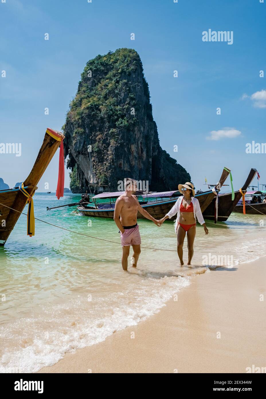couple mid age on a tropical beach in Thailand, tourist on a white tropical beach, Railay beach with on the background longtail boat. Railay Beach in Krabi province. Ao Nang, Thailand. Stock Photo