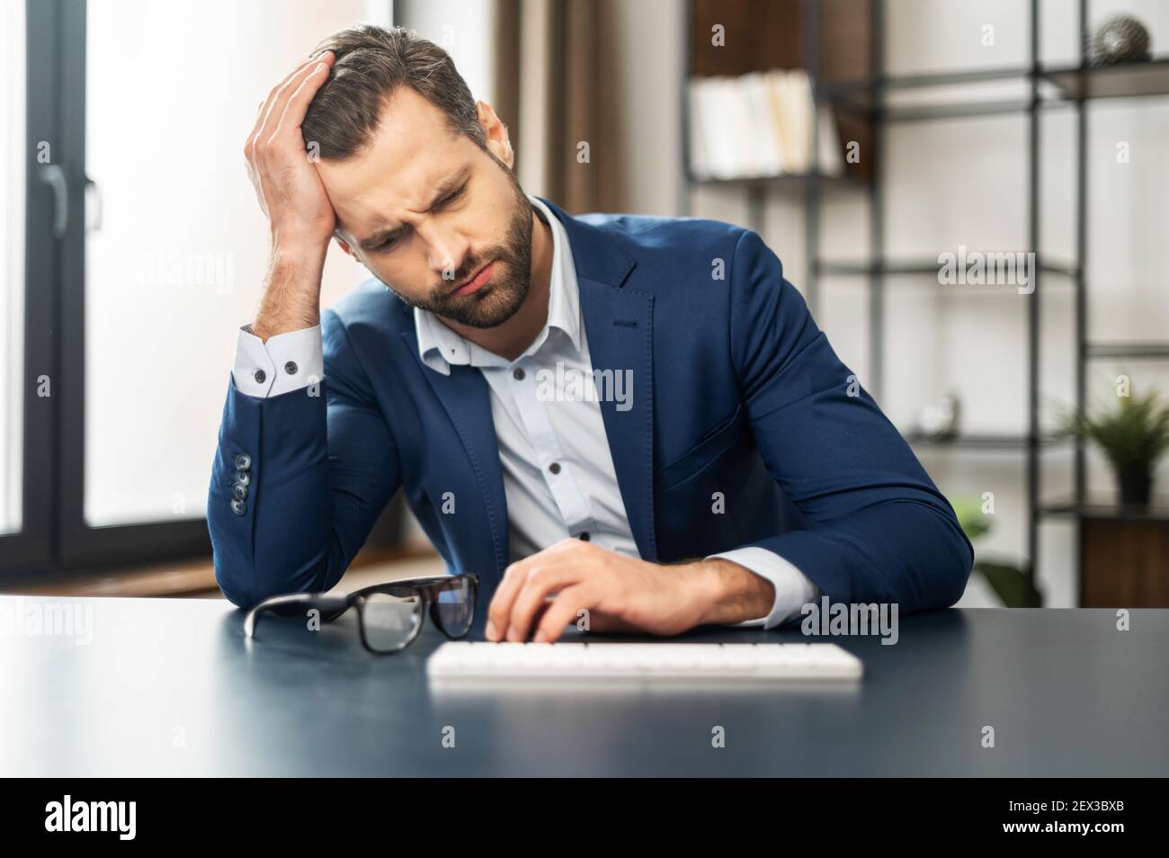Mature exhausted businessman thinking about budget and future of his company, overworked, bankrupt, unmotivated man sitting at keyboard, feeling stress and disinterest in work, lost the court case Stock Photo