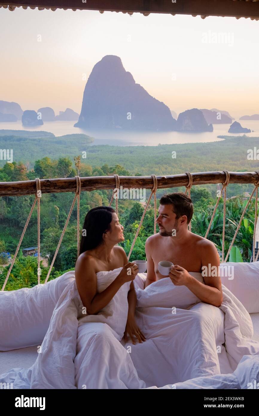 Phangnga Bay, couple waking up in bed in nature jungle looking out over ocean and jungle during sunrise at the wooden hut in the mountains of Thailand men and woman mid age morning sunrise Phanga Thailand Stock Photo