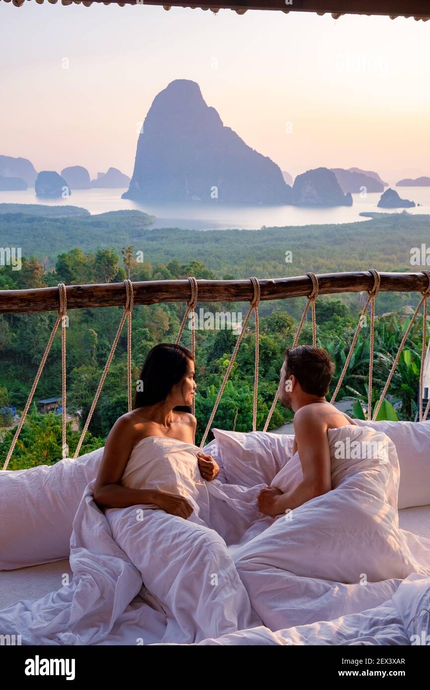 Phangnga Bay, couple waking up in bed in nature jungle looking out over ocean and jungle during sunrise at the wooden hut in the mountains of Thailand men and woman mid age morning sunrise Phanga Thailand Stock Photo