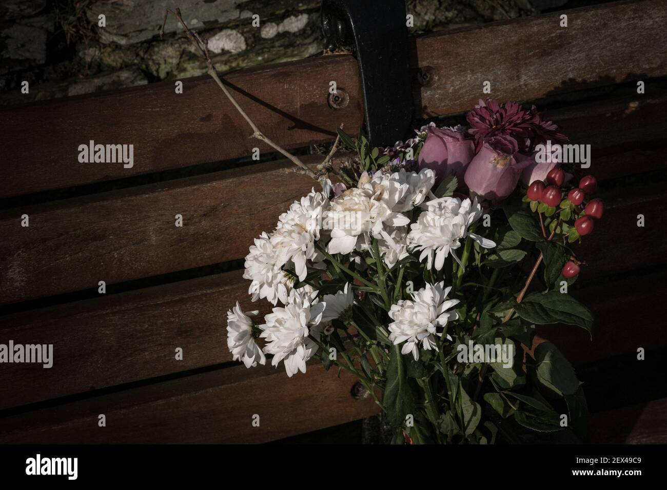 A bouquet of wilting flowers left on a bench in remebrance. Stock Photo