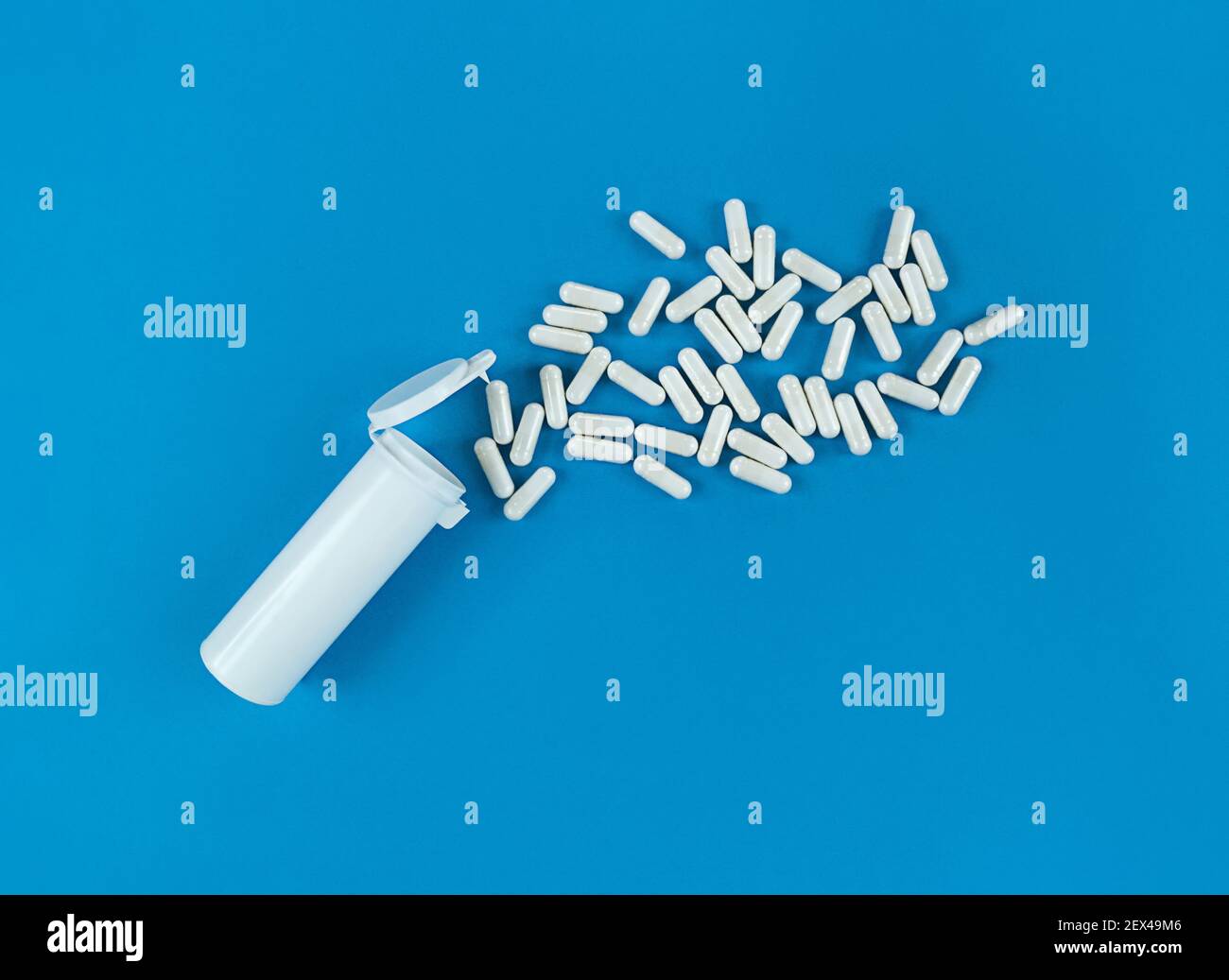 White plastik medical bottle and scattered pills capsules on blue backdrop with copy space. Stock Photo