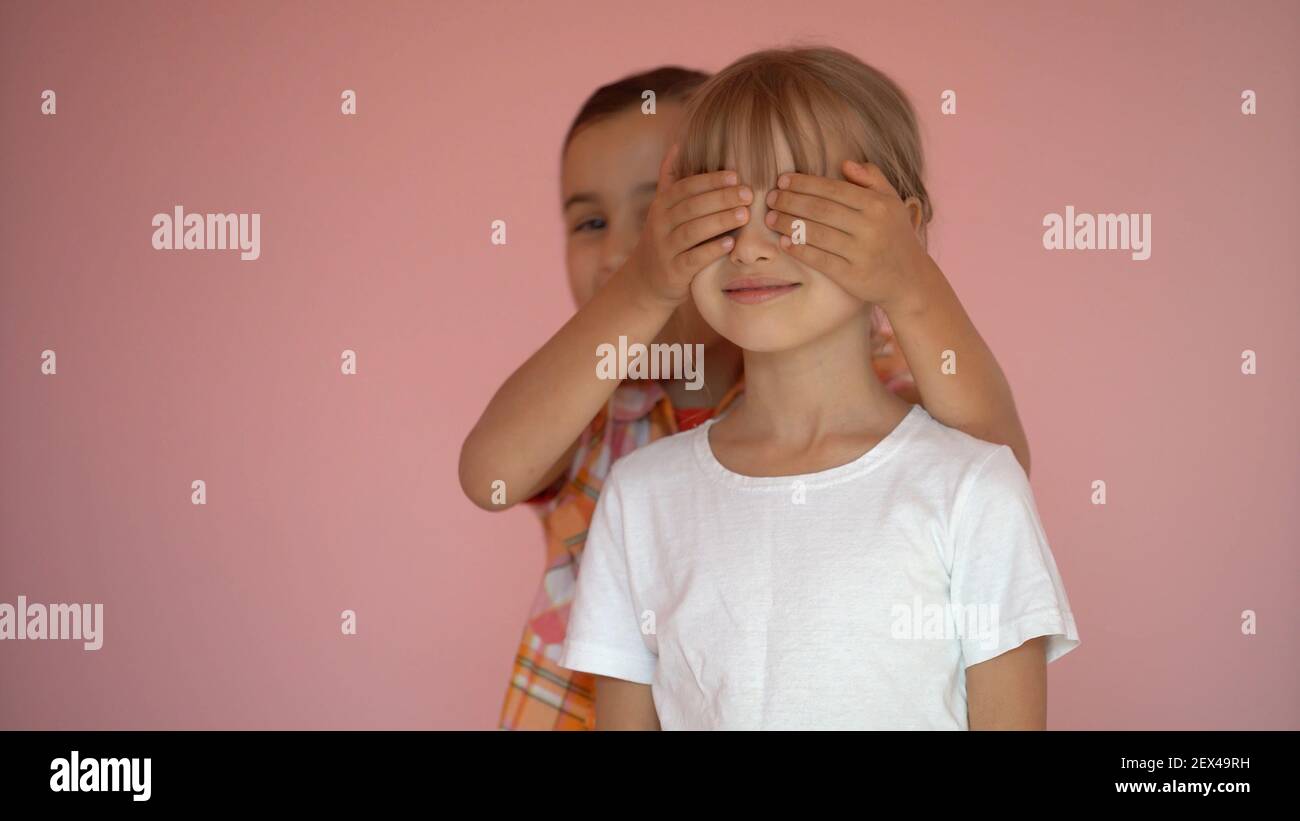 Portrait of two cute friends 7 years old girl Covering Eyes Isolated over pink background Stock Photo