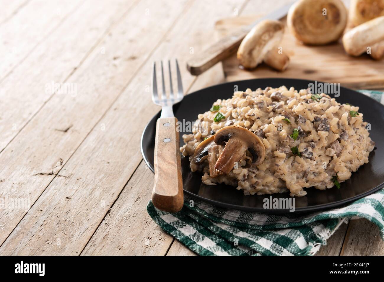 Risotto with mushroom on black plate on wooden table.Copy space Stock Photo