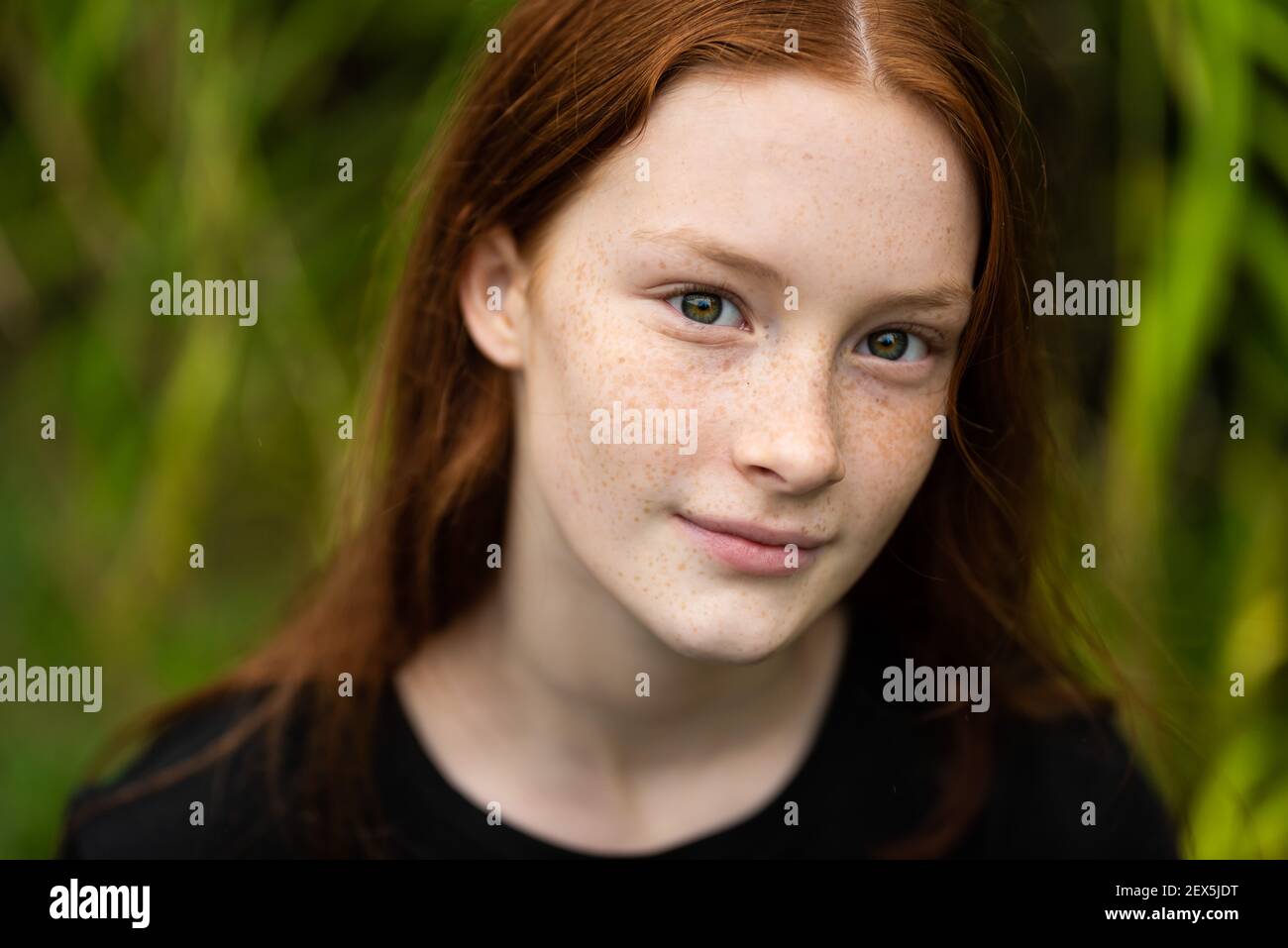 Red haired twelve year old girl with freckles posing with a nature bokeh background Stock Photo