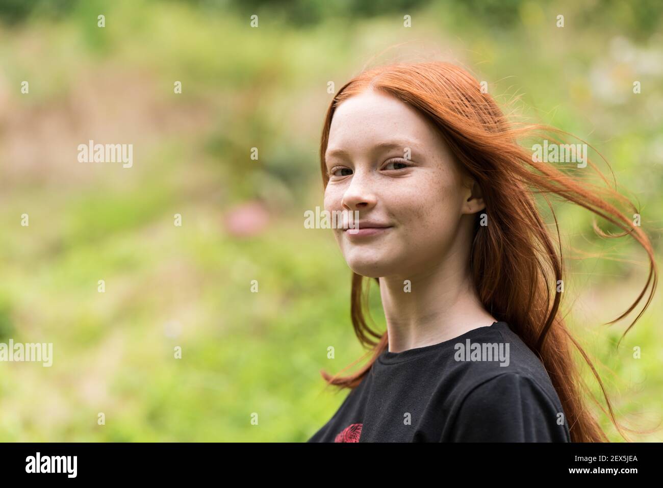 Red haired twelve year old girl with freckles posing with a nature bokeh background Stock Photo