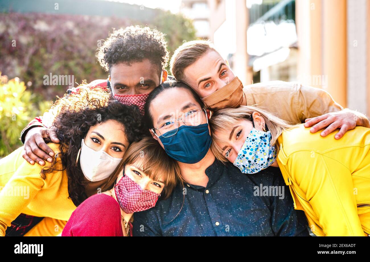 Multicultural milenial friends taking selfie smiling behind face masks - New normal friendship and life style concept with young people having fun Stock Photo