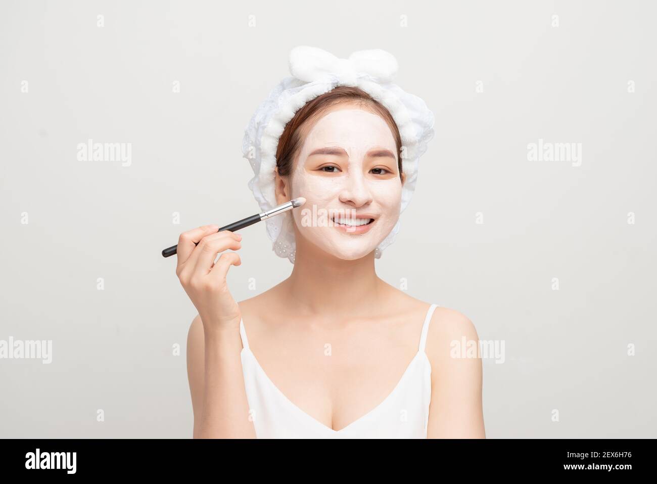 Skin care. Female applying black purifying mud mask, cosmetic healing clay to half face, using brush. Beauty and wellness. Spa and acne treatment. Stock Photo