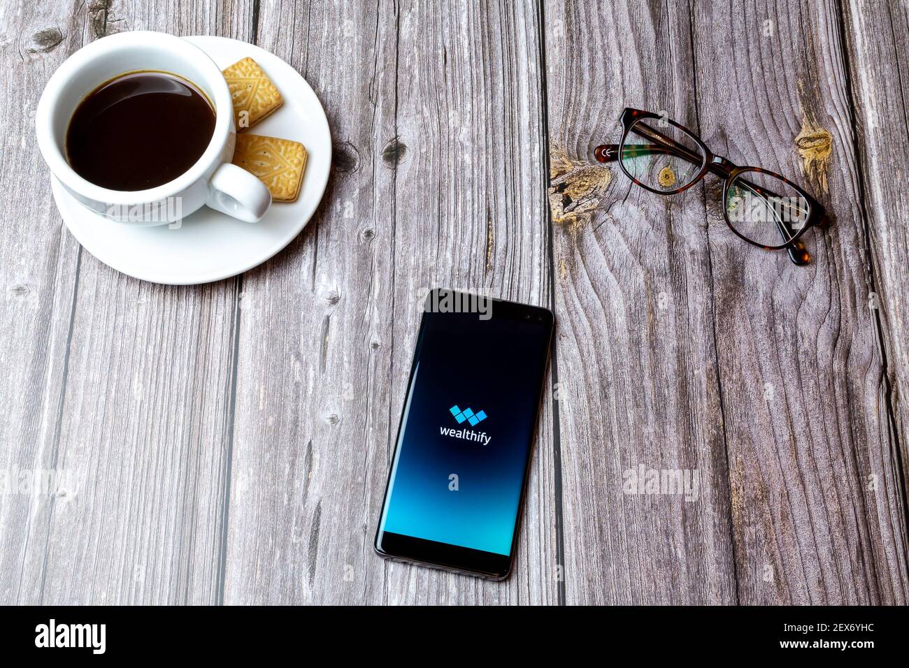 A mobile phone or cell phone laid on a wooden table with the Wealthify savings app open next to a coffee Stock Photo
