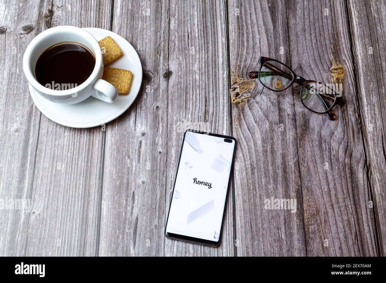 A mobile phone or cell phone laid on a wooden table with the Honey Shopping app open next to a coffee Stock Photo