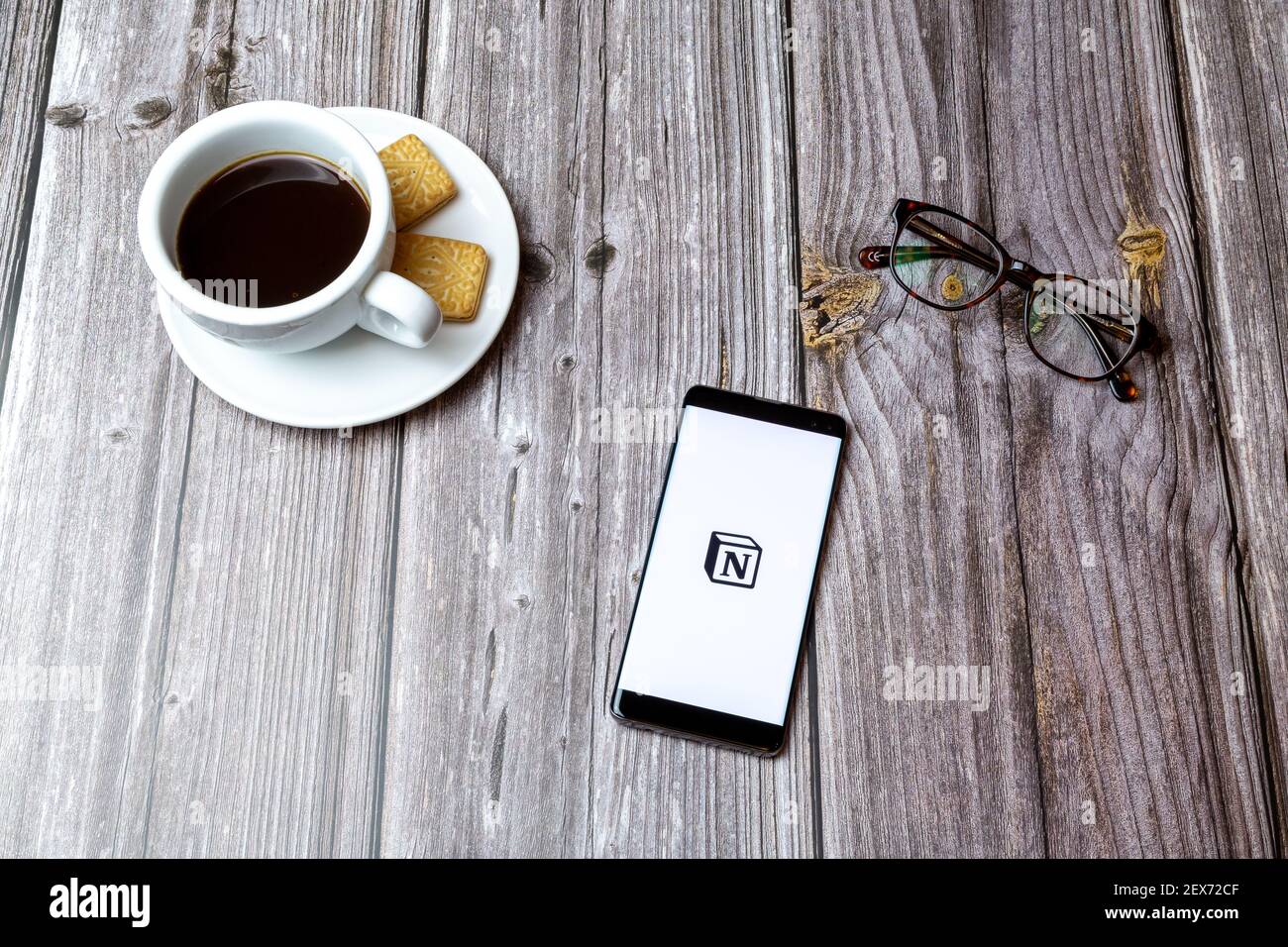 A mobile phone or cell phone laid on a wooden table with the Notion notes app open next to a coffee Stock Photo