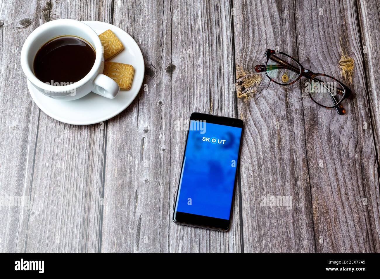 A mobile phone or cell phone laid on a wooden table with the Skout dating app open next to a coffee Stock Photo