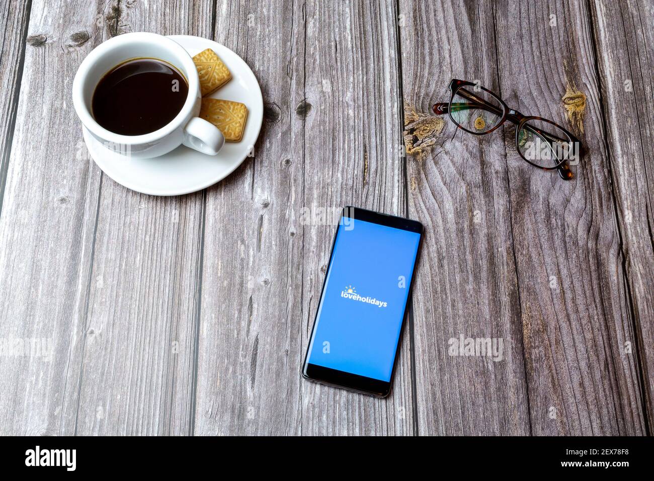 A mobile phone or cell phone laid on a wooden table with the Loveholidays app open next to a coffee Stock Photo